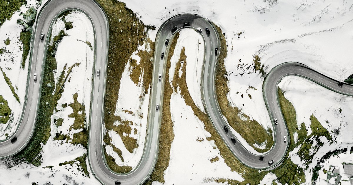Luchtfoto van auto's op een bochtige bergweg met haarspeldbochten tussen de sneeuw op de Julierpas in Zwitserland