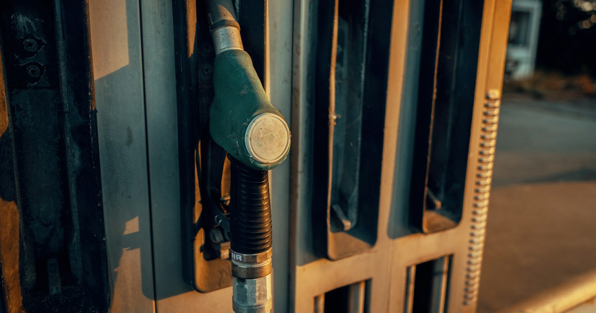 Groen vulpistool in de houder van een brandstofpomp bij een tankstation, in het licht van de ondergaande zon