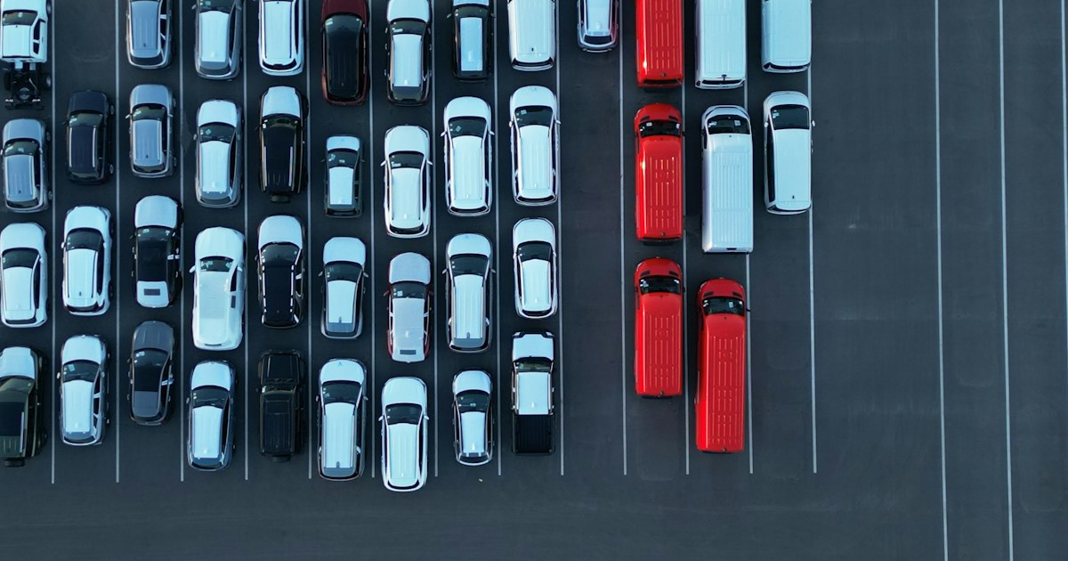 Luchtfoto van rijen geparkeerde personenauto's en rode en witte bestelbussen op een parkeerterrein