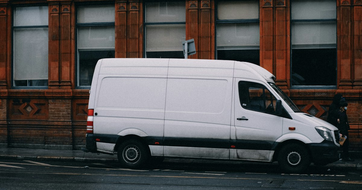 Witte bestelbus van opzij, geparkeerd langs de weg voor een bakstenen gebouw