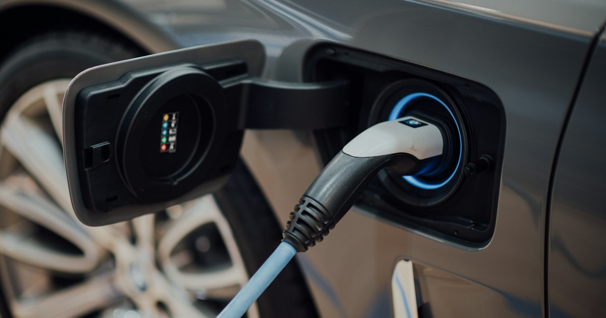 Laadstekker met blauwe kabel in de laadpoort van een grijze elektrische auto