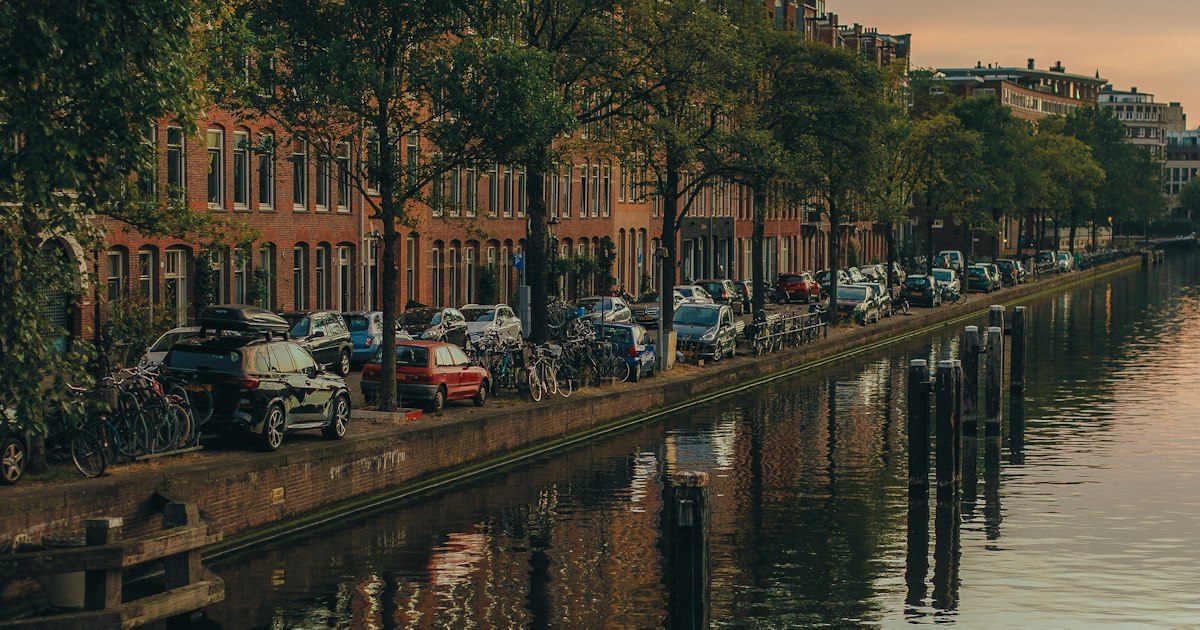 Geparkeerde auto's en fietsen langs een gracht in Amsterdam bij zonsondergang