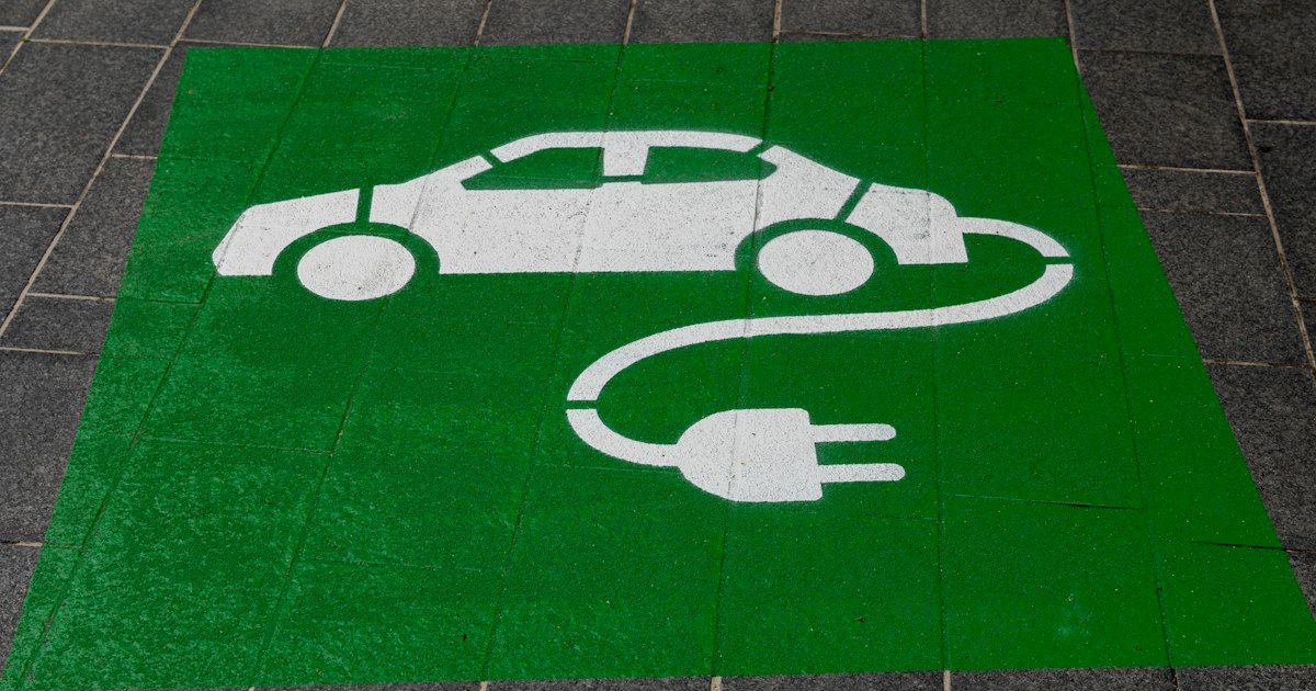 Groen vlak met een wit symbool van een auto met laadkabel en stekker, geschilderd op een parkeerplaats