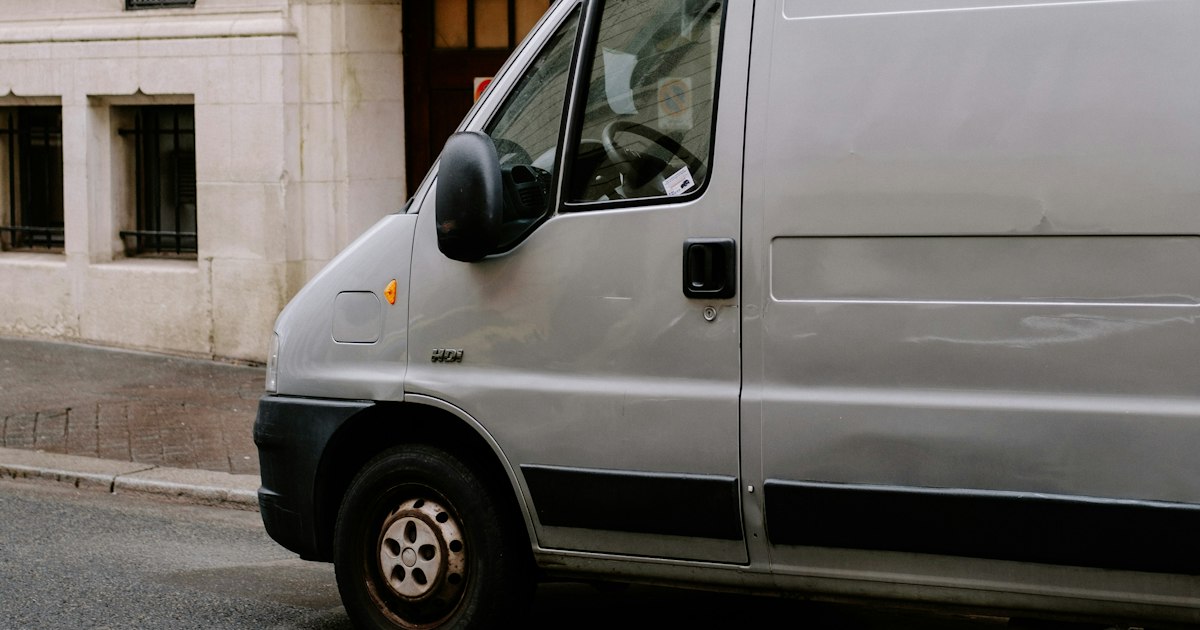 Grijze bestelbus geparkeerd langs de stoep voor een stenen gebouw in een stadsstraat